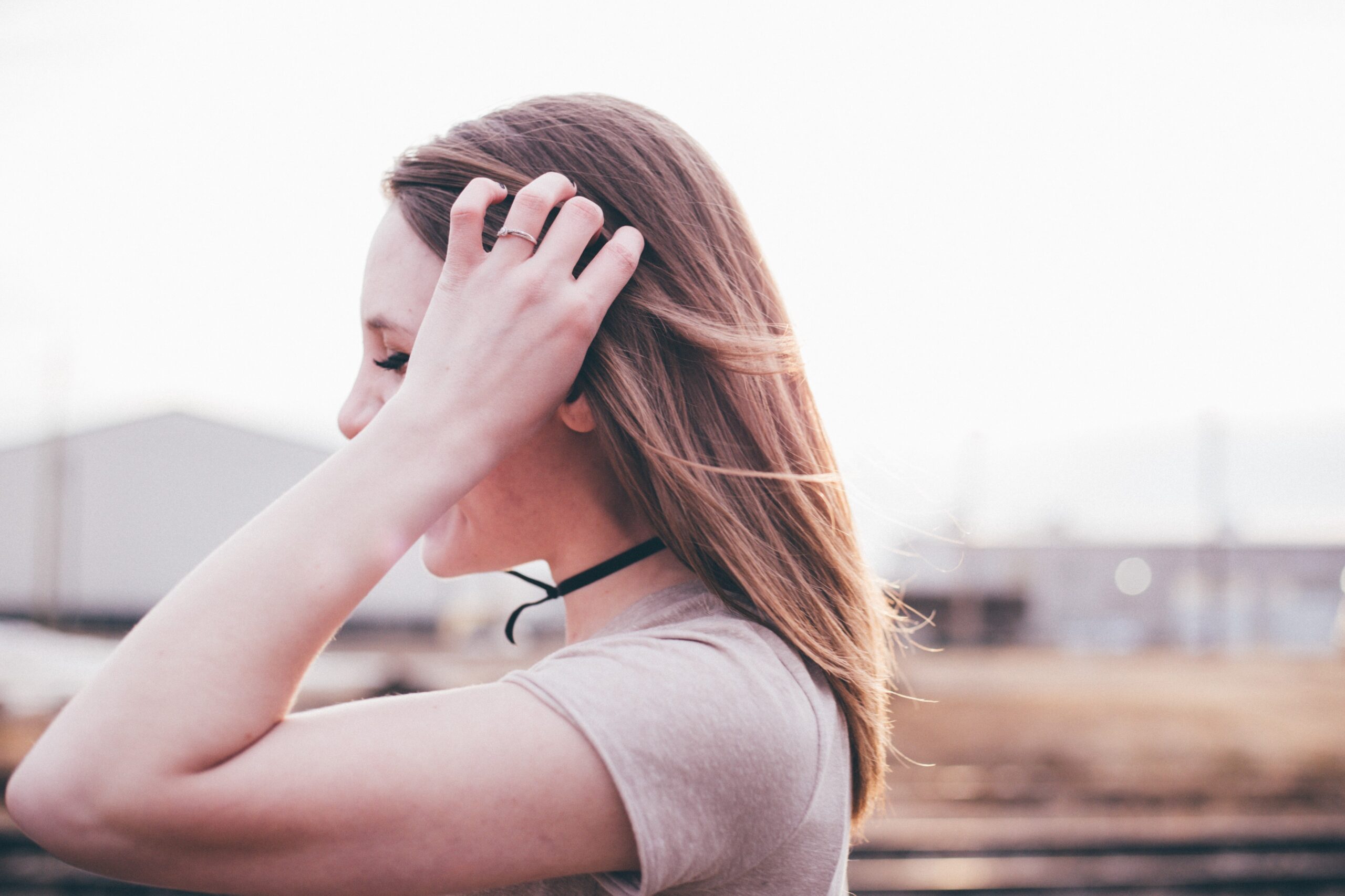 Woman with one hand in her hair, viewed from the side outdoors.